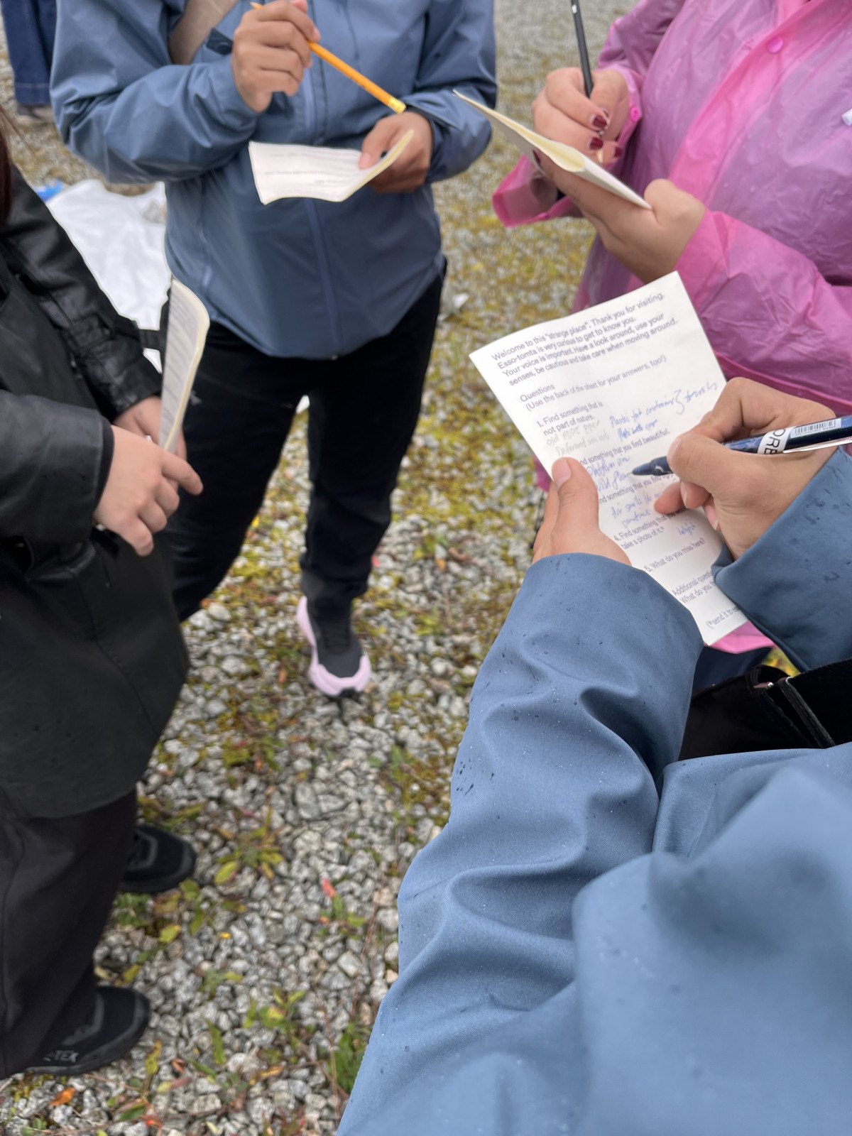 four people standing together closely and filling out forms on paper