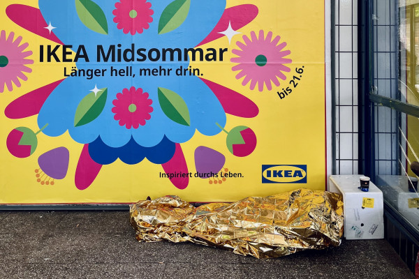 Person mit goldener Rettungsdecke vor einem IKEA-Werbeplakat im &ouml;ffentlichen Raum